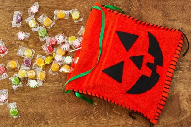 A pile of candy and a homemade jack-o-lantern treat bag made from washcloths and felt fabric.